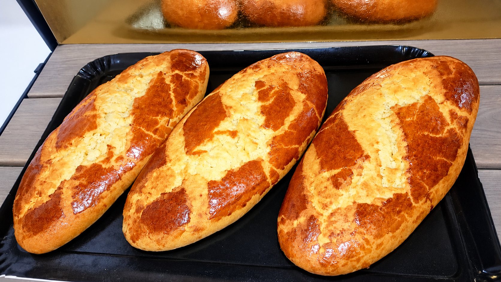 Trois pains dorés à la croûte craquelée posés sur un plateau noir.